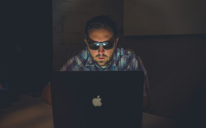 person on computer in the dark with sunglasses