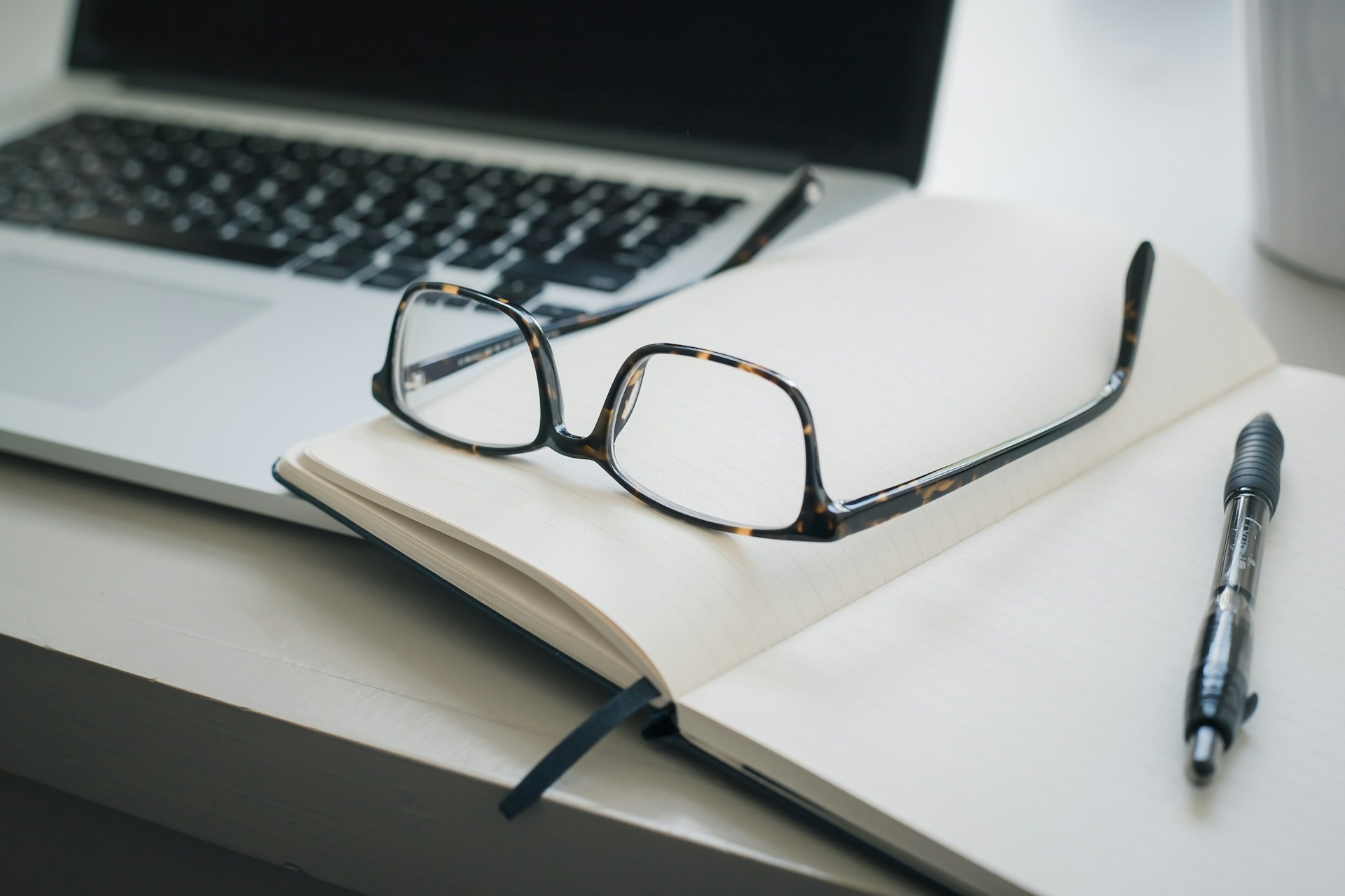 Glasses and a notebook beside a MacBook laptop